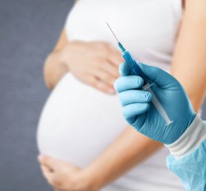 Idea of vaccination for pregnant women - doctor's gloved hand holding a syringe in front of a pregnant woman