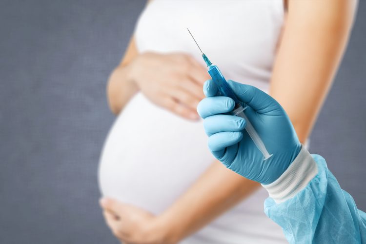Idea of vaccination for pregnant women - doctor's gloved hand holding a syringe in front of a pregnant woman