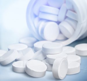round white tablets spilling out of a white pill bottle onto a light blue background