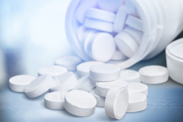 round white tablets spilling out of a white pill bottle onto a light blue background
